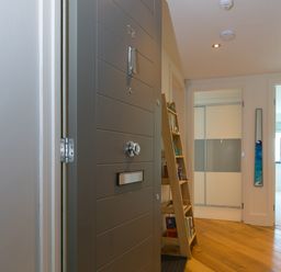 An open grey front door leading to a hallway with wooden floor a leaning wooden bookshelf and white doors at Crystal Bay in St Ives