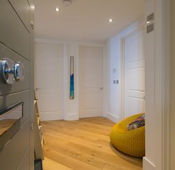 A hallway with three white doors a yellow round chair with a pillow and wooden floor at Crystal Bay in St Ives