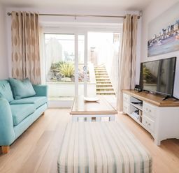 A living room with a blue sofa table and striped ottoman in front of a sliding glass door at 16 Ocean Heights in Newquay