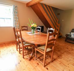 A dining area with a wooden table and six chairs next to a window and wooden stairs in a living space at Teach Chiuin in Coolaheen near Cappoquin County Waterford