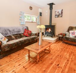 A living room with a wooden floor a sofa an armchair a coffee table with flowers and a wood burning stove at Teach Chiuin in Coolaheen near Cappoquin County Waterford