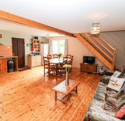 An open living room and kitchen with wooden floors a dining table chairs a wooden coffee table a sofa and a television under wooden stairs at Teach Chiuin Coolaheen near Cappoquin County Waterford