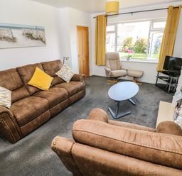 A living room with brown sofas yellow curtains a gray armchair and a blue round coffee table at 53 St Brides View in Roch