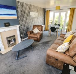 A living room with brown sofas a coffee table fireplace dining table and chairs with yellow curtains at 53 St Brides View in Roch