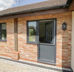 A brick exterior wall with a blue door and two windows at Garden Cottage in Upton Upon Severn