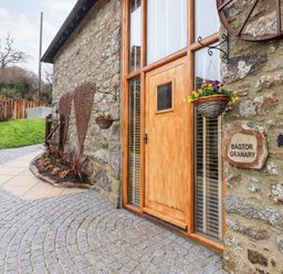Stone building exterior with wooden door flower baskets and cobblestone path at Bagtor Granary in Ilsington