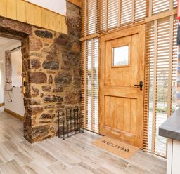 A wooden door with window and welcome mat near a stone wall and kitchen countertop at Bagtor Granary in Ilsington