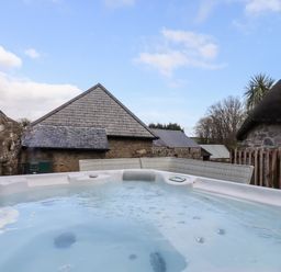An outdoor hot tub with buildings and a wooden fence in the background at Bagtor Granary in Ilsington