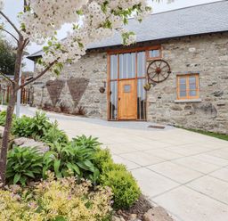 A stone building with wooden windows and door with a paved driveway and flowering tree in front at Bagtor Granary in Ilsington