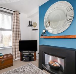 A living room corner with a television on a stand next to a window with curtains and a chest on the floor at Penmar in Looe