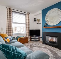 A living room with a blue sofa cushions a rug television and a fireplace at Penmar in Looe
