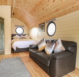 A room with a bed and a black sofa with pillows wooden floor and walls at Filbert Pod in Arundel West Sussex