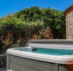 An outdoor hot tub surrounded by plants and a stone wall at Filbert Pod in Arundel West Sussex