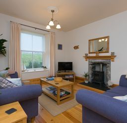 A living room with two blue sofas a wooden coffee table a fireplace a television and a window with curtains at Chynance in Porthcurno