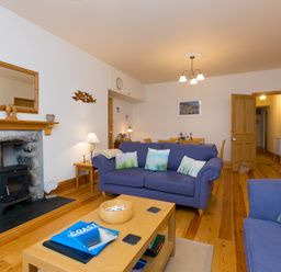 A living room with blue sofas a coffee table and a fireplace at Chynance in Porthcurno