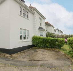 A white two story house with black trim and green hedges in front at Chynance in Porthcurno