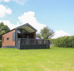 A small cabin with a deck surrounded by grass and hedges at Jacob's Meadow Pod 2 Minsterley near Chirbury