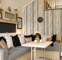 A living room with a corner sofa a table and a clock on the patterned wall at Jacobs Meadow Pod 2 in Minsterley near Chirbury