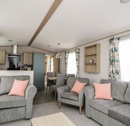 A living room with grey sofas and pink cushions next to a dining area with a wooden table and grey chairs at Burlees Nest in Brigham near Great Broughton Cockermouth