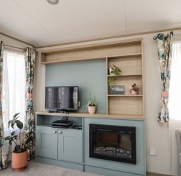 A living room with a TV on a cabinet and a fireplace with potted plants and curtains at Burlees Nest in Brigham near Great Broughton Cockermouth
