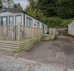An exterior view of a mobile home with a wooden deck and paved driveway at Burlees Nest in Brigham near Great Broughton Cockermouth