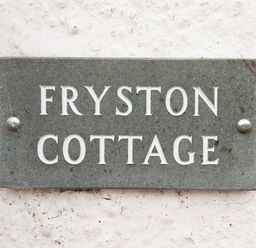 A stone plaque with the words Fryston Cottage mounted on a white textured wall at Fryston Cottage in Keswick