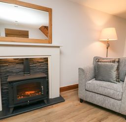 A fireplace with a mirror above and a gray armchair with cushions next to a floor lamp at Fryston Cottage in Keswick
