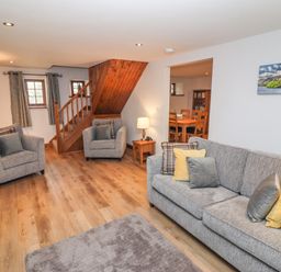 A living room with two armchairs a sofa with pillows a wooden staircase and a dining area at Fryston Cottage in Keswick