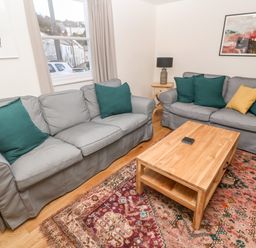 A living room with two grey sofas with green and yellow cushions a wooden coffee table a patterned rug and wall art at Widgeons Keel in Flushing