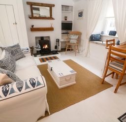 A living room with a white sofa and patterned cushions a wooden chair a fireplace and a wooden table at The Little Net Loft Mousehole near Penzance