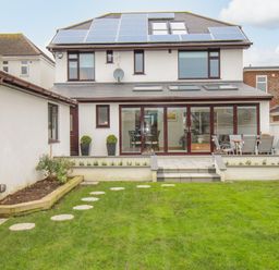 A backyard with a lawn and stepping stones leading to a patio with outdoor furniture and solar panels on the house roof at Family House in Weymouth