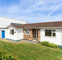 A single-story house with a tiled roof and stone entrance surrounded by a grassy yard at Zapadiah in Polzeath
