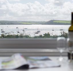 A window view of boats on water with hills in the background and a table with a wine bottle and glasses in the foreground at 4 The Terrace in Rock