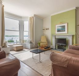 A living room with armchairs a coffee table a fireplace a television and a bay window overlooking water at 4 The Terrace Rock