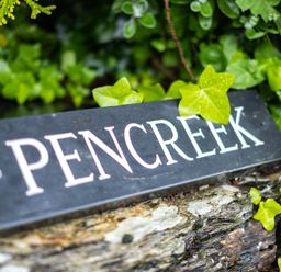 A black sign with the word Pencreek surrounded by green leaves and placed on a stone surface at Pencreek in Rock