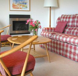 A living room with wooden armchairs a round wooden coffee table with flowers a plaid sofa and a wall-mounted fireplace at Rosevallen in Daymer Bay