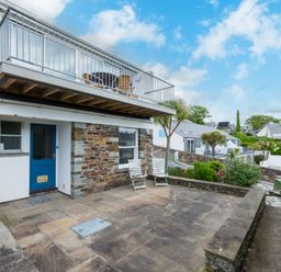 Exterior view of a house with blue door stone walls a patio with two chairs and a balcony above at Slipway 7 Rock