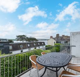 A balcony with a metal table and four chairs overlooking rooftops and water at Slipway 7 in Rock