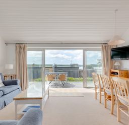 A living room with blue sofas a wooden dining table with chairs and a glass coffee table with sliding doors leading to an outdoor seating area at Slipway 7 in Rock