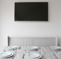 A dining table set with plates glasses and cutlery below a wall mounted television at Slipway 10 in Rock