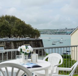 A balcony with white plastic chairs and a table with flowers a book and a glass overlooking boats on water at Slipway 10 in Rock