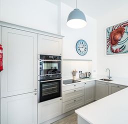 A kitchen with white cabinets built in oven stove sink clock and crab painting at Slipway 10 in Rock