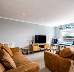A living room with brown sofas a wooden TV stand a flat screen TV and a window seat with cushions at Slipway 15 in Rock