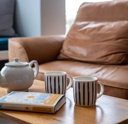 A wooden table with a white teapot two striped mugs and a book in front of a brown leather sofa at Slipway 15 in Rock