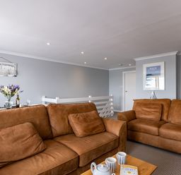 A living room with brown sofas a wooden coffee table with cups and teapot and a dining table with flowers at Slipway 15 in Rock