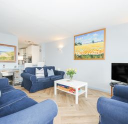 A living room with blue sofas a white coffee table with board games a TV and paintings on the walls at Slipway 16 in Rock