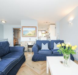 A living room with blue sofas a white coffee table with yellow flowers and a painting above a fireplace at Slipway 16 in Rock