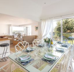 A dining area with glass table set for six and chairs next to a balcony and an open living room with sofas at Slipway 19 in Rock