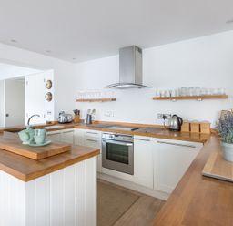 A kitchen with wooden countertops white cabinets a stove and kitchen utensils at Slipway 19 in Rock