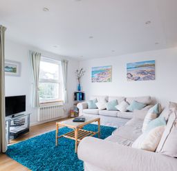 A living room with two beige sofas and blue cushions a blue rug a glass TV stand with a TV and a wooden coffee table at Slipway 21 in Rock